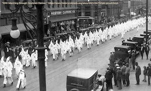 Ku Klux Klan members in white hoods and robes marching through the streets of Denver.